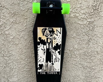 May include: Black longboard skateboard with green wheels. The deck features a black and white graphic of a tarot card, "The Tower."