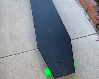 May include: A black longboard skateboard with green wheels. The skateboard is on a gray concrete surface.