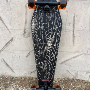 May include: Black longboard skateboard with a black and white spiderweb design on the deck. The skateboard has orange wheels and black trucks.