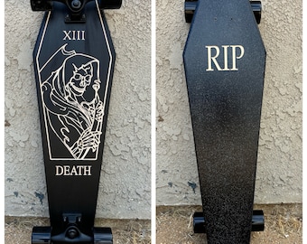 May include: Black skateboard shaped like a coffin with a graphic of the Grim Reaper and the words "XIII" and "DEATH". The back of the skateboard has the word "RIP" written on it.