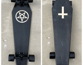 May include: Black skateboard with black wheels and black trucks. The deck is shaped like a coffin and has a gold cross on the top. The bottom of the deck has a pentagram.