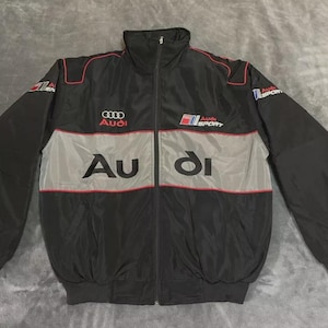 May include: Black and gray Audi Sport jacket with red accents. The jacket features the Audi logo and "Audi Sport" text. The front has a full zipper and a high collar. The sleeves are long and the jacket is made of a lightweight material.