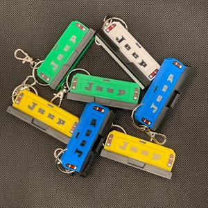 May include: A collection of Jeep-themed keychains in various colors, including green, white, blue, and yellow. Each keychain features the word "Jeep" and a small silver keyring.