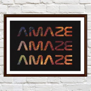 Op de afbeelding: Ingelijste kunst met het woord "AMAZE" driemaal herhaald in een pixelachtig, verlopend ontwerp. De letters gaan over van blauw naar oranje en geel tegen een zwarte achtergrond. Het kunstwerk zit in een donkerbruine lijst.