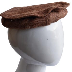 May include: A brown wool cap with a flat top and a curved brim. The cap is worn on a white mannequin head.