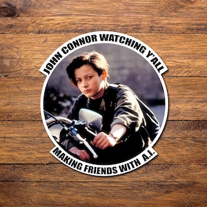 May include: A black and white circular sticker with the text "John Connor Watching Y'all Making Friends With A.I." around the edge. The center of the sticker features a photo of a young boy riding a motorcycle.