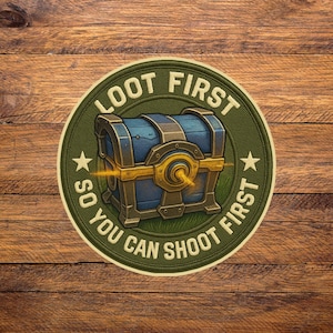 May include: A round patch with the text "LOOT FIRST SO YOU CAN SHOOT FIRST" encircling a blue treasure chest with gold accents. The patch is green with two stars on either side of the chest, set against a wooden background.