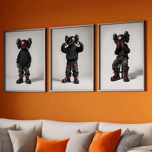 May include: Three framed prints of black and red cartoon figures with a white background. The prints are hanging on an orange wall above a white sectional sofa with orange throw pillows.