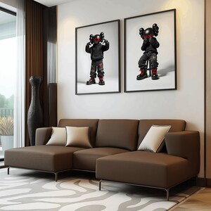 May include: A brown sectional sofa with two pillows, positioned in front of a white wall with two black framed prints of cartoon figures.