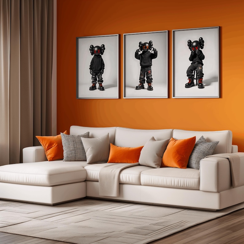 May include: Three framed prints of black and red cartoon figures with a white background. The prints are hanging on an orange wall above a white sectional sofa with orange throw pillows.