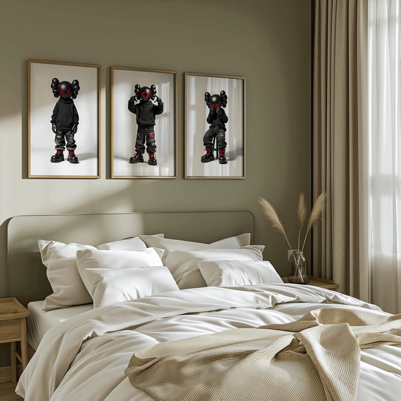 May include: Three framed prints of black and red cartoon figures wearing black clothing and red shoes. The prints are hanging on a light green wall above a white bed with white bedding and a tan throw blanket.