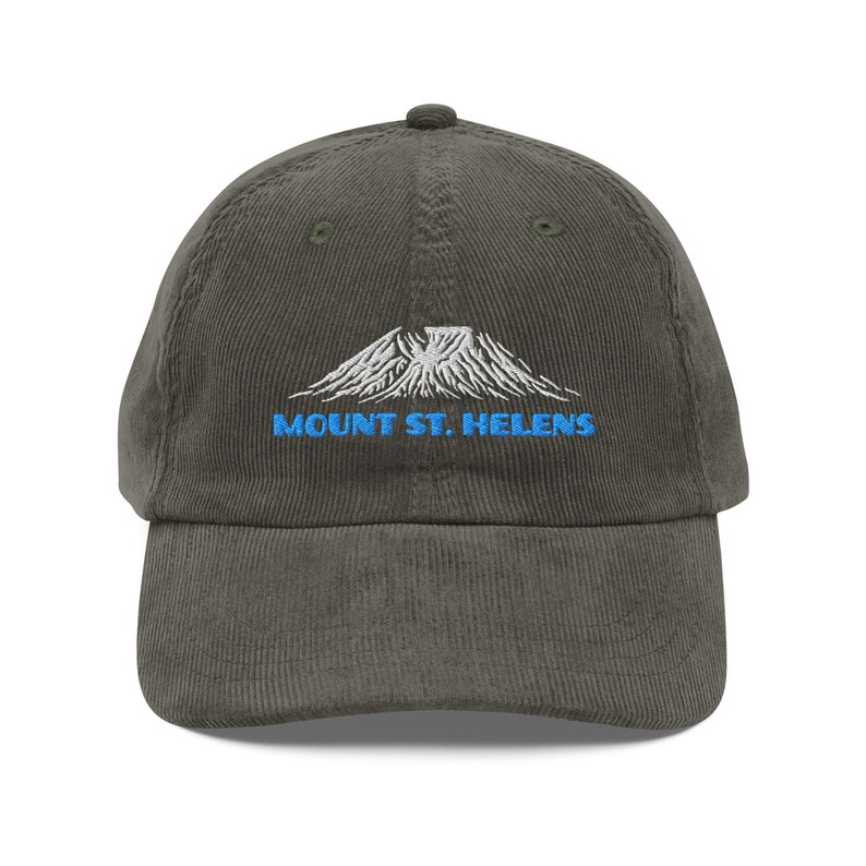 May include: Olive green corduroy baseball cap with a curved brim. The cap features an embroidered design of a mountain and the text "MOUNT ST. HELENS" in blue. The cap has a structured crown and an adjustable strap.