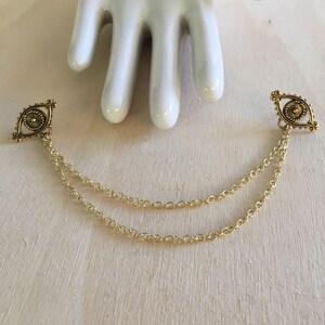 May include: A pair of gold-tone eye charm pendants connected by a double chain.