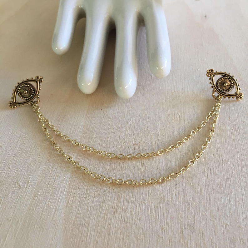 May include: A pair of gold-tone eye charm pendants connected by a double chain.