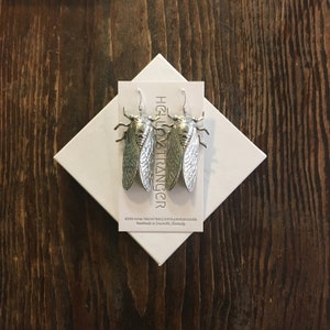 May include: Silver cicada earrings on a white card with the text "Hello Stranger" and "etsy.com/shop/hellostrangergoods Handmade in Louisville, Kentucky".