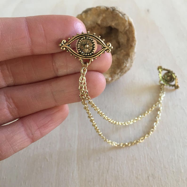May include: Gold tone eye charm with a detailed design, hanging from a double chain.