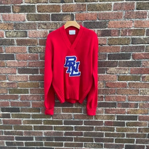 May include: Red v-neck sweater with a blue and white felt patch that says "B.N.L."