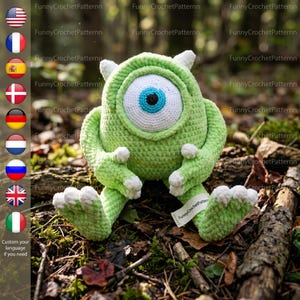 Puede incluir: Un monstruo verde tejido a crochet con un gran ojo azul, detalles blancos y pequeños cuernos. El peluche está sentado sobre hojas y ramitas. La etiqueta dice "FunnyCrochetPatternn".