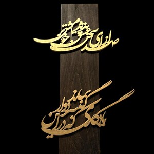 May include: A wooden plaque with two gold-colored, ornate calligraphic designs. The plaque is dark brown, and the background is black. The calligraphy appears to be in a script style, with flowing lines and curves.