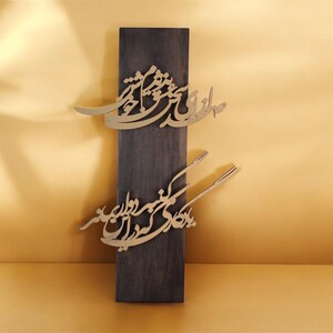 May include: A dark wooden rectangular plaque with gold-colored calligraphy. The calligraphy is in two sections, one near the top and one near the bottom. The background is a warm, golden color.