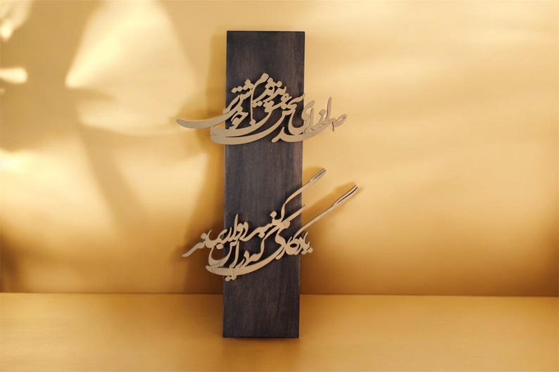 May include: A dark wooden rectangular plaque with gold-colored calligraphy. The calligraphy is in two sections, one near the top and one near the bottom. The background is a warm, golden color.