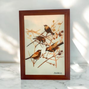 May include: A framed artwork featuring a nature scene with four brown birds perched on branches with small brown flowers. The artwork is signed "Remarkable 2014" in the bottom right corner.