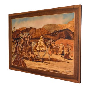 May include: A framed artwork depicting a desert scene with figures on foot and horseback. The artwork is crafted from various wood tones, creating a detailed landscape with mountains and a blue sky. The frame is a dark brown wood.