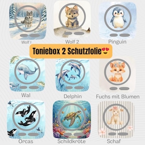 Könnte beinhalten: Eine Auswahl an Schutzfolien für die Toniebox 2, jeweils mit einer Aquarellillustration. Designs umfassen einen Wolf, einen Pinguin, eine Delfinfamilie, einen Fuchs mit Blumen, Orcas, eine Meeresschildkröte und ein Schaf.