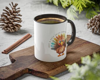 May include: White ceramic coffee mug with a black rim and handle. The mug has a colorful illustration of a turkey with the text "Just a cute chick avoiding..." printed on the front.