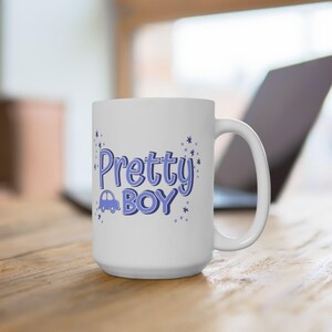 Puede incluir: Una taza de cerámica blanca con el texto Pretty BOY en fuente morada, un pequeño icono de coche morado y detalles en forma de estrella. El diseño está centrado en la parte frontal de la taza, que cuenta con un asa estándar y forma cilíndrica.