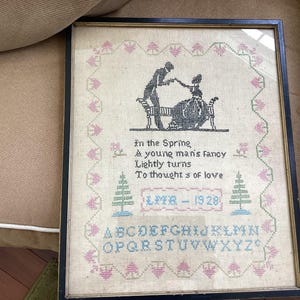 May include: Framed vintage cross-stitch sampler with a black silhouette of a couple on a bench. The sampler includes the text "In the Spring & young man's fancy Lightly turns To thoughts of love" and the year 1928.