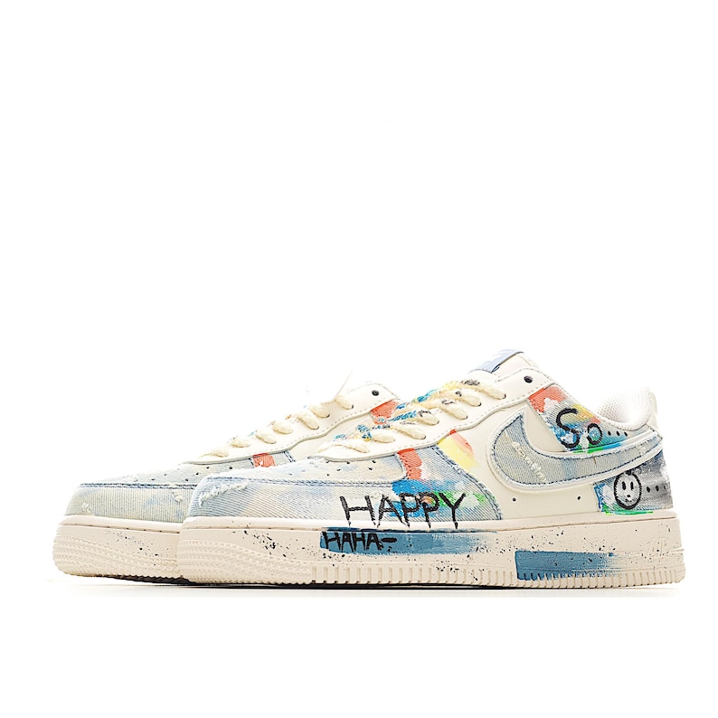 Puede incluir: Zapatillas de color crema con salpicaduras de pintura coloridas y detalles de mezclilla. Las zapatillas presentan las palabras "HAPPY" y "HAHA" en negro, junto con un dise&ntilde;o de carita sonriente. Las suelas tienen un dise&ntilde;o moteado.