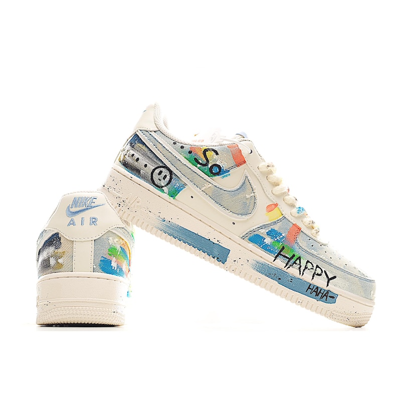 Puede incluir: Zapatillas Nike Air Force 1 blancas y azules con arte de graffiti personalizado. Las zapatillas presentan una carita sonriente, la palabra "So" y las palabras "HAPPY HAHA" en negro. Los zapatos tienen un patr&oacute;n similar al denim y acentos coloridos.