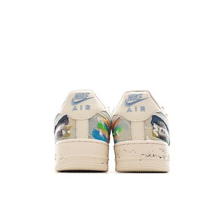 Puede incluir: Par de zapatillas Nike Air Force 1 color crema. Las leng&uuml;etas del tal&oacute;n presentan el logotipo de Nike y la palabra "AIR" en azul. Los laterales de los zapatos tienen salpicaduras de pintura abstractas coloridas. Las suelas son blanquecinas con un aspecto desgastado.
