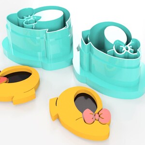 May include: A set of cookie cutters in the shape of a shoe with a bow. The cutters are yellow with a pink bow and black interior. Two teal-colored cutters are also present. These are likely for baking or crafting.