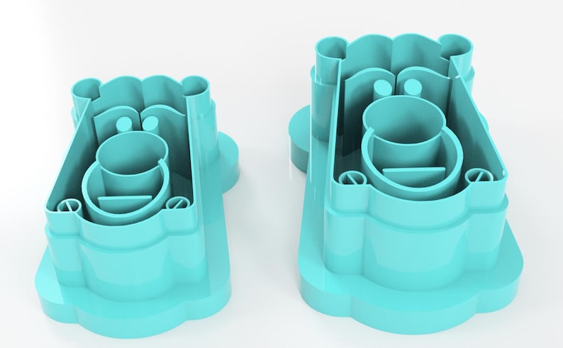 May include: Two turquoise plastic cookie cutters. Each cutter has a rounded base with a scalloped edge, a central circular cup, and a series of vertical and curved supports. The cutters are designed to create a bear shape.