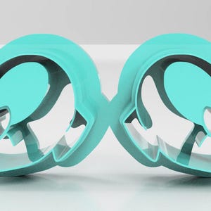 May include: Two turquoise cookie cutters in the shape of a hat with a bow. The cutters are made of plastic and have a smooth, glossy finish. The design is symmetrical, with each cutter mirroring the other.