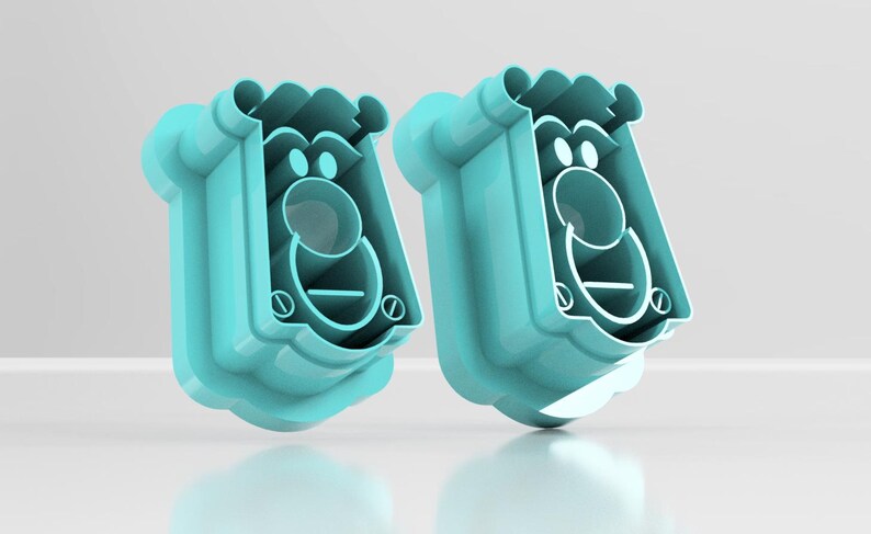 May include: Two turquoise-colored, cartoon-like face-shaped cookie cutters. Each cutter has a rounded top, a circular nose, and a curved mouth. The design includes eye and mouth details, and a decorative bottom edge.