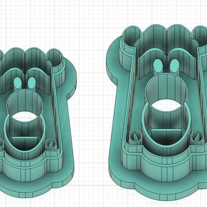 May include: Two teal-colored cookie cutters. The cutters have a rectangular shape with a circular opening in the center and rounded edges. The top of the cutter has a wavy design, and there are two small circular cutouts near the top.