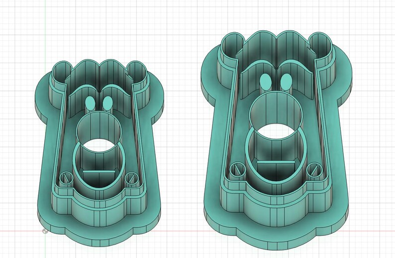 May include: Two teal-colored cookie cutters. The cutters have a rectangular shape with a circular opening in the center and rounded edges. The top of the cutter has a wavy design, and there are two small circular cutouts near the top.