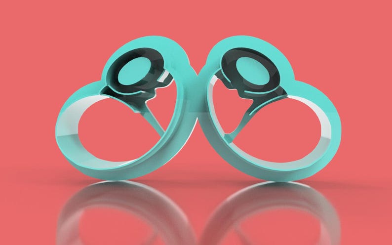 May include: A pair of teal-colored, heart-shaped objects with black and gray circular accents. The objects are mirrored, with a reflective surface below against a coral background. The design is modern and abstract.
