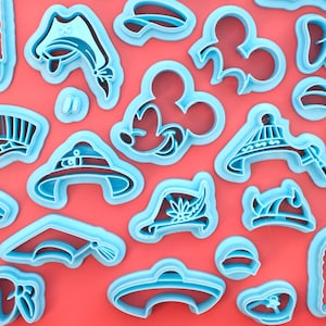 May include: A collection of light blue plastic cookie cutters in various shapes, including hats, a Mickey Mouse head, and other themed designs. The cutters are arranged on a red background, creating a playful and colorful display.