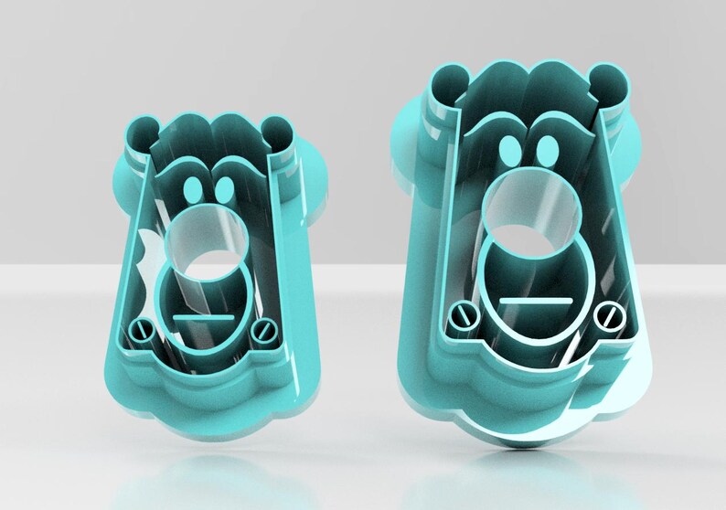 May include: Two turquoise plastic cookie cutters in the shape of a bear's face. The cutters have a circular opening for the mouth and two smaller circles for the eyes. The bear's face has a rounded top and a scalloped bottom.