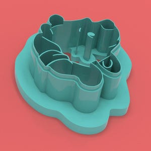 May include: A teal-colored cookie cutter in the shape of a bear. The cutter has a detailed design with rounded edges and a handle. The bear is sitting down. The cutter is on a red background.