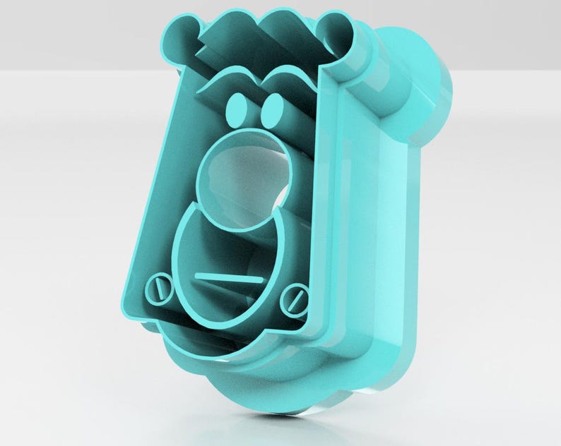 May include: A light blue plastic cookie cutter in the shape of a cartoon face. The cutter has a rectangular body with a rounded top and a circular opening for the mouth. Two small circles form the eyes, and a horizontal line represents the mouth.