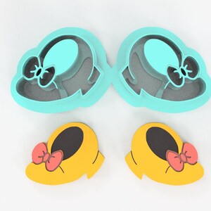 May include: A set of four cookie cutters in a whimsical design. Two are shaped like hats with bows, and two are shaped like yellow shoes with red bows. The cutters are made of plastic and are on a white background.