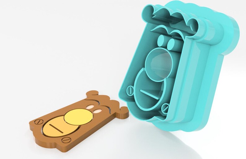 May include: A two-part cookie cutter set. The brown cookie has a yellow circle and a line. The blue mold has a matching shape. The set is designed to cut out a bear-shaped cookie.