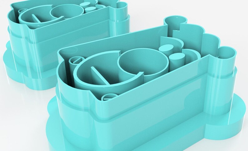 May include: Two turquoise plastic cookie cutters. Each cutter has a rounded base with a scalloped edge and a complex interior design featuring curved and cylindrical shapes. The cutters are designed for baking.
