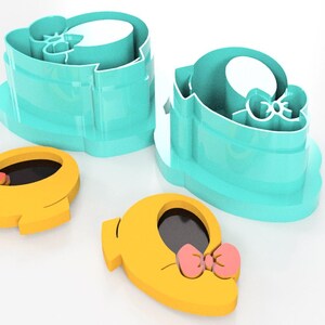 May include: A set of turquoise cookie cutters shaped like a baby shoe with a bow, alongside two yellow cookie cutouts with pink bows. The cutters are designed for baking and crafting.