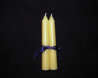 May include: Two yellow beeswax candles tied together with a purple ribbon.